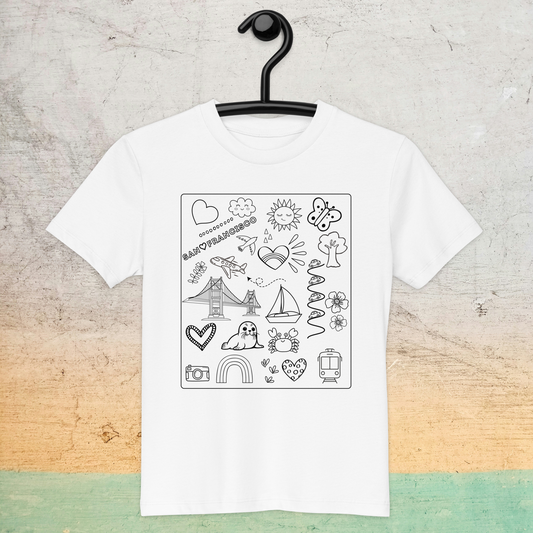 A white San Francisco Color-in Tee: Organic cotton kids t-shirt by byKath.com hangs on a black hanger against a textured background. The shirt features black line art drawings, including a rainbow, lighthouse, Eiffel Tower, boat, dog, butterfly, sun, cloud, and various other playful doodles.