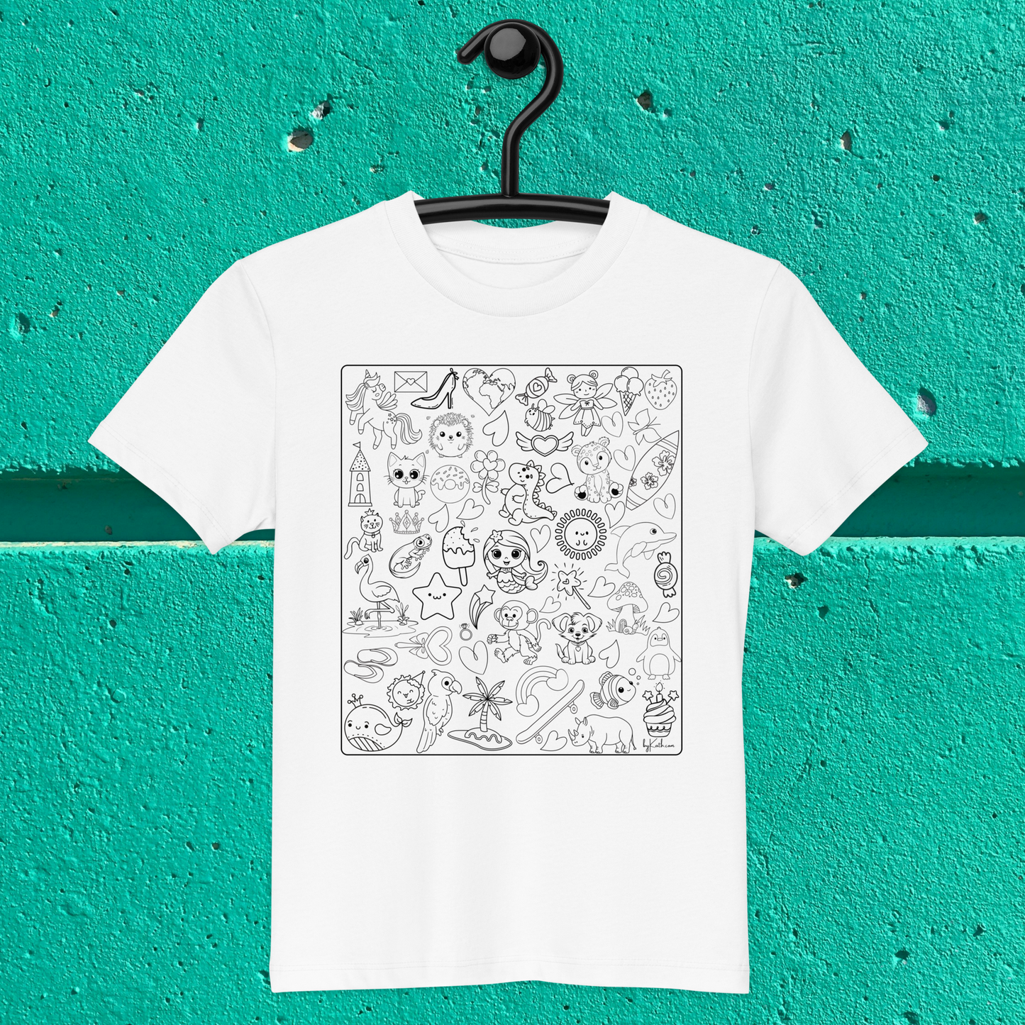 A white Happy Doodles Color-in Tee by byKath.com hangs on a black hanger against a bright teal wall. This organic cotton kids t-shirt features a square design filled with various black and white doodles, including cute animals, flowers, stars, food, and abstract shapes—perfect for creative activities and mindful moments.